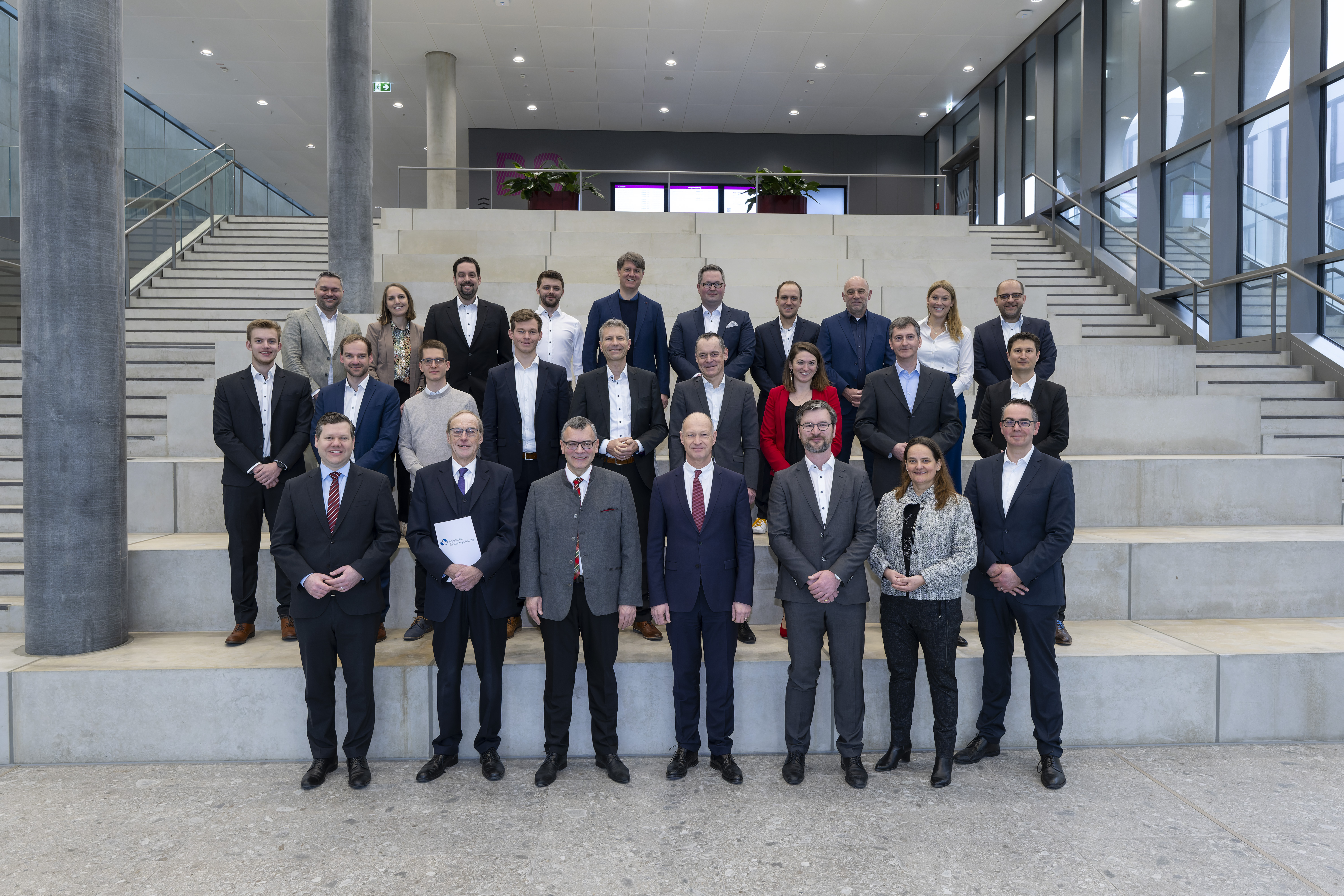 Projektteam mit Staatsminister Dr. Florian Herrmann und Prof. Dr. Dr. h.c. (NAS RA) Arndt Bode (erste Reihe, dritter bzw. zweiter von links) bei der Bescheidübergabe (Bild: Stephan Görlich / Flughafen München)